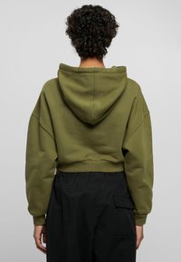 Cropped olive green hoodie with a drawstring hood, wide sleeves, and ribbed cuffs. The texture is smooth with a solid color and minimal detailing.