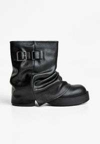 Zwarte leren enkellaars met een slouch-ontwerp, voorzien van een zilveren gesp-accent en een dikke rubberen zool voor extra stabiliteit.