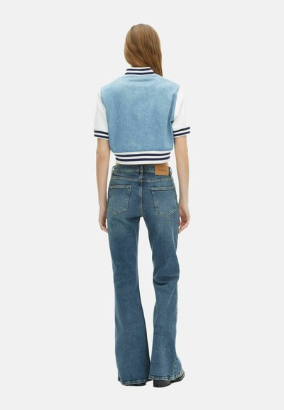 Krótka dżinsowa kurtka w jasnoniebieskim kolorze z białymi rękawami i granatowymi paskami, zestawiona z dżinsami w kolorze niebieskim z szerokimi nogawkami, posiadającymi brązową skórzaną metkę.