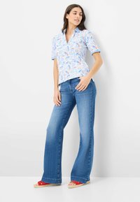 Camicia a maniche corte con un motivo di foglie blu, abbinata a jeans a zampa d'elefante azzurri chiari. Indossata con espadrillas rosse e naturali.