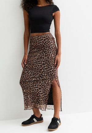 Haut noir court à manches courtes, associé à une jupe maxi imprimée léopard avec une fente sur le côté et un tissu léger et texturé.