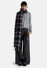 Szara, puszysta, skrócona kurtka, czarne plisowane spodnie z ekologicznej skóry oraz długi kraciasty szalik w ciemnozielone i fioletowe odcienie.