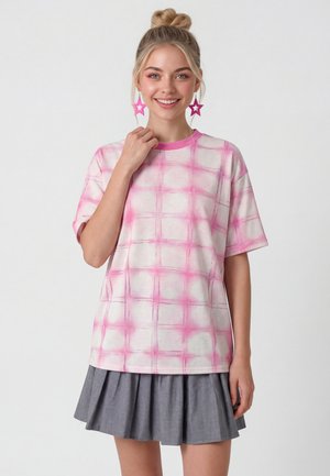 Nuori nainen hymyilee, pukeutuneena vaaleanpunavalkoraidalliseen t-paitaan, harmaaseen pliseerattuun hameeseen, vaaleanpunaisiin tähtimuotoisiin korvakoruihin, vaaleat hiukset nutturalla.