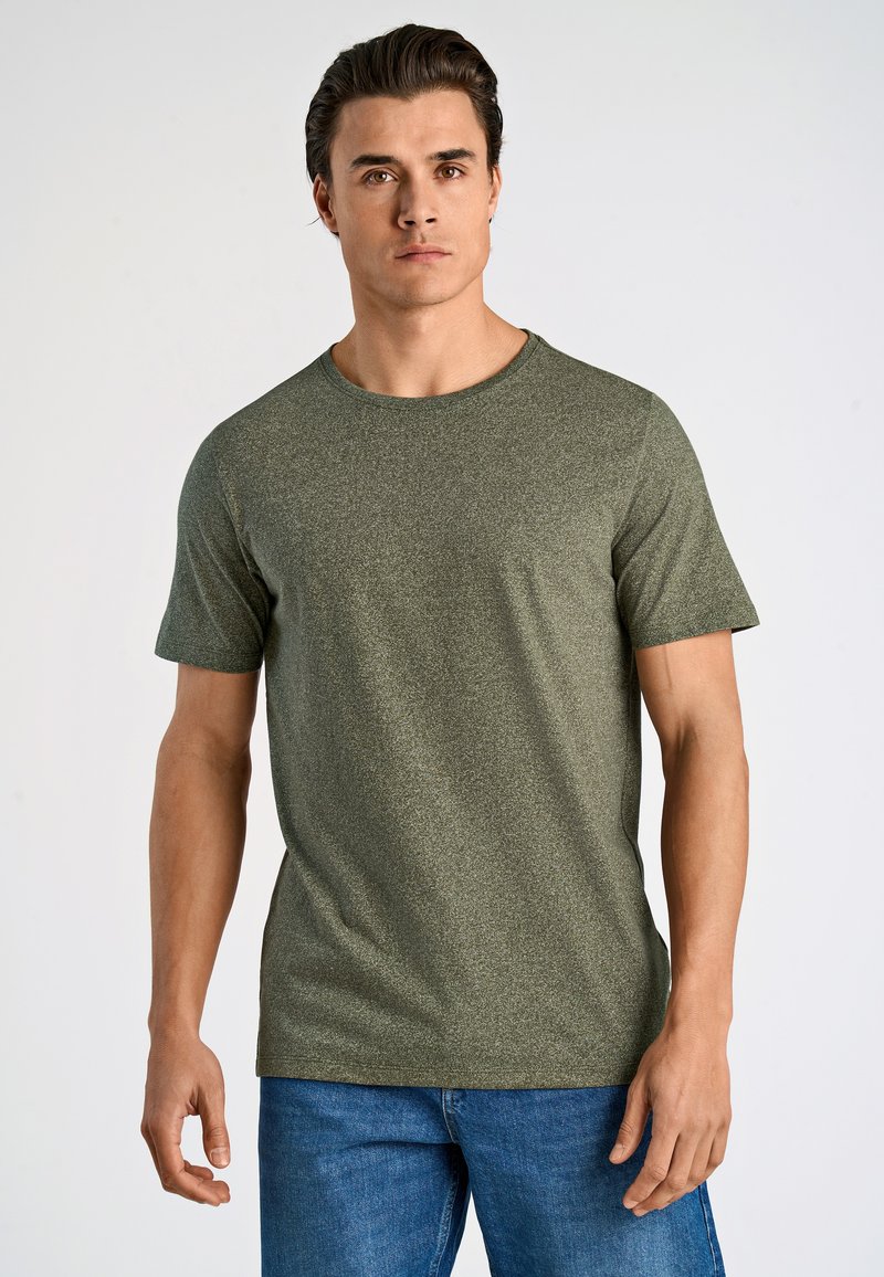 Oliwkowa koszulka z krótkim rękawem, wykonana z teksturowanej tkaniny, z okrągłym dekoltem i prostym krojem. W połączeniu z niebieskimi dżinsami.