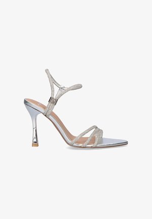 Sandalia plateada de tacón alto con tiras finas y brillantes, una correa en el tobillo con una hebilla pequeña y un diseño de punta puntiaguda.