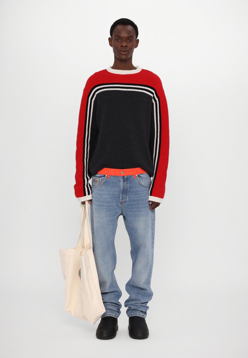 Chunky strikkegenser i rød, svart og hvit; lys blå jeans; klar oransje belte; svarte slip-on sko; lerret totebag.