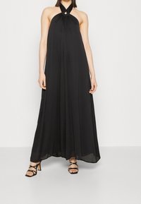 Abito maxi nero con scollo all'americana e dettaglio a chiave nella scollatura, tessuto fluido e design a strati, abbinato a sandali con tacco a strappo.