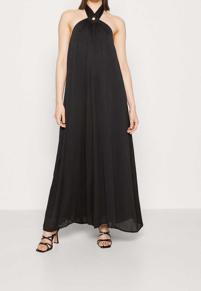 Abito maxi nero con scollo all'americana e dettaglio a chiave nella scollatura, tessuto fluido e design a strati, abbinato a sandali con tacco a strappo.