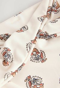 Světle béžová látka má složitý květinový vzor v odstínech oranžové, modré a černé. Design je hladký s jemnou, splývavou strukturou.