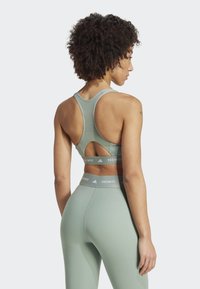 Sujetador deportivo verde claro con diseño de espalda racer, detalle de corte y banda elástica TechFit; combinado con leggins de cintura alta a juego.