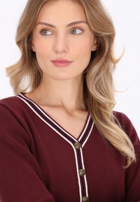 Burgundy knitted cardigan with a v-neck, white and navy striped trim, and four gold buttons. Features long sleeves and a textured finish.