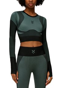 Dunkelgrünes langärmliges Cropped-Top mit schwarzen Akzenten, verfügt über ein tailliertes Design, strukturierte Materialien und ein Logo auf der Brust. Passende hoch taillierte Leggings.