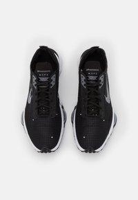 Czarne sportowe buty z teksturowaną cholewką, sznurowanym designem i białymi akcentami. Posiadają zaokrągloną podeszwę z przezroczystą jednostką amortyzującą.