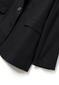 Blazer noir avec revers cranté, deux poches avant, une fermeture à un bouton et une texture de tissu lisse.