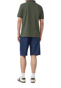 Groene poloshirt met korte mouwen, gecombineerd met denim shorts. De outfit wordt compleet gemaakt met witte sneakers en crew-lengte sokken.