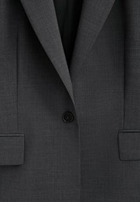 Blazer grigio scuro con tessuto texturizzato, rever a punta, e chiusura con un singolo bottone nero, dotato di tasche laterali e vestibilità sartoriale.