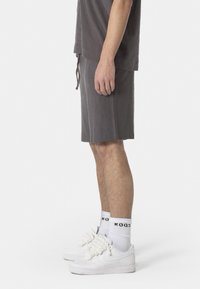 Graue, leichte Baumwollshorts mit einem elastischen Bund, Seitentaschen und einer lässigen Passform, kombiniert mit weißen Sneakern und Socken.