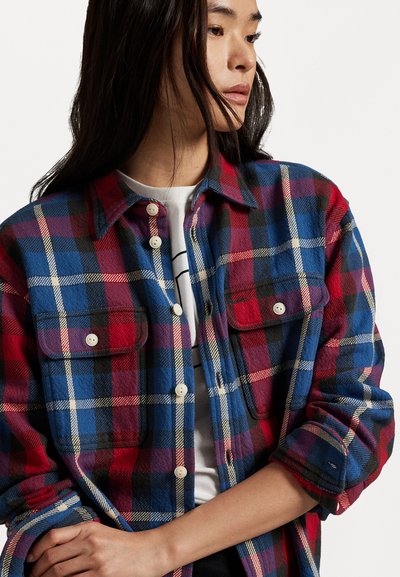 Red, blue, and black plaid flannel shirt with button-up front, two chest pockets, and roll-up sleeves. Soft texture and lightweight design.