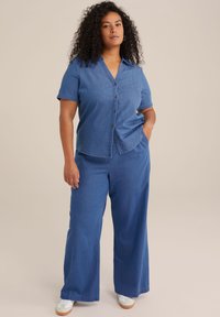 Ensemble en denim composé d'une chemise à manches courtes avec bouton et de pantalons larges dans une teinte de bleu clair harmonieuse, avec une texture lisse et un design décontracté.
