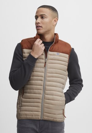 Gepolstertes Weste mit einem beige Oberteil und braunen Schultern, ausgestattet mit einem Reißverschluss, Stehkragen und seitlichen Taschen mit Zuglaschen.
