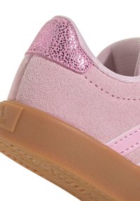 Roza suede tenisica s blistavim roza akcentom na peti i teksturiranom gumenom potplatu. Sadrži roza šivane detalje i glatku tkaninu podstava.