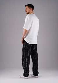 White oversized t-shirt, black pants with vertical white streaks, and white sneakers. Plain texture, relaxed fit, and casual design.