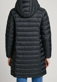 Svart, lång vadderad kappa med huva och horisontell sömnad. Har en mjuk yta och rak passform, som når mitt på låret.