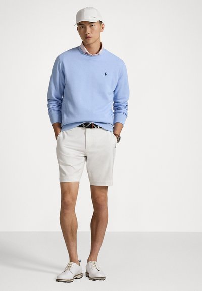 Pull bleu clair, shorts blancs et chaussures blanches. La tenue comprend une casquette blanche et une ceinture à motifs. Design simple, look formel-décontracté.