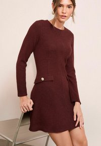 Mauve pletena haljina s dugim rukavima, teksturirani materijal, usko tijelo, lepršava suknja i dvije bočne džepove sa okruglim gumbima.