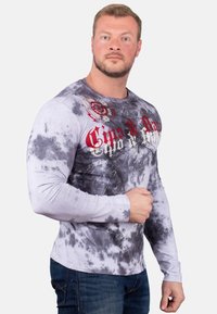 Langarm-Tie-Dye-Shirt in Grau und Weiß mit rotem grafischem Text. Verfügt über ein körpernahes Design und einen weichen, strukturierten Stoff.