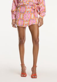 Korte jurk in een levendige roze, oranje en blauwe paisleyprint. Kenmerkt lange mouwen, een strik taille en is gecombineerd met oranje hakken met banden.