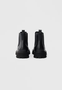 Bottines en cuir noir avec panneaux latéraux élastiques et languettes, dotées d'une semelle épaisse à motif texturé pour une meilleure adhérence.