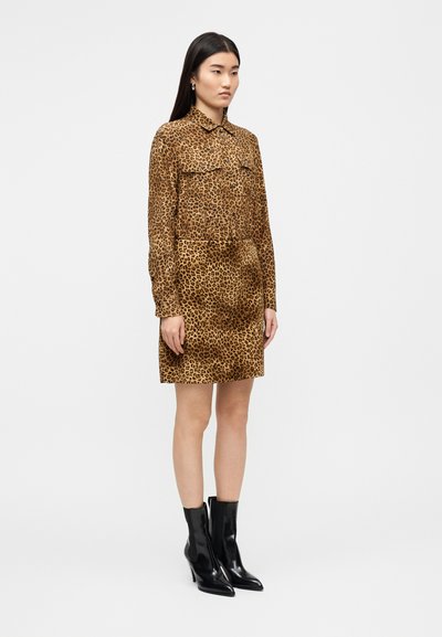 Φόρεμα πουκαμίσα με μοτίβο λεοπάρ σε αποχρώσεις καφέ και ταν, με κουμπιά μπροστά, μακριά μανίκια και πλαϊνές τσέπες. Συνδυασμένο με μαύρα μποτάκια στον αστράγαλο.