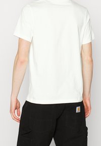 Vit bomullströja med regular fit, korta ärmar och rund halsringning, kombinerad med svarta cargobyxor med sidofickor och en logotypapplikation.