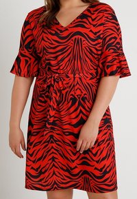 Vestido estampado en rojo y negro con mangas cortas, escote en forma de V y cintura con lazo. La tela tiene una textura suave y presenta un audaz diseño de rayas de cebra.