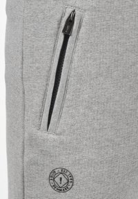 Grijze joggerpants van een gestructureerde stof, met een ritszak, zwart logo-label en contrasterende stiksels langs de naden.