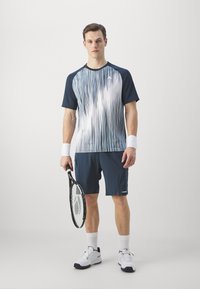 Marineblaues Kurzarm-Sportshirt mit weißen vertikalen Streifen, kombiniert mit marineblauen Shorts. Weiße Handgelenkbänder und ein Tennisschläger in der Hand.