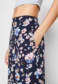 Floral print trousers in navy, made from lightweight fabric. Features colorful flower designs, side pockets, and a smooth waistband.