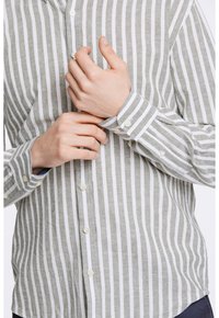 Camisa de botón a rayas en lino verde y blanco, con cuello, mangas largas y puños abotonados. Tejido texturizado con rayas verticales.