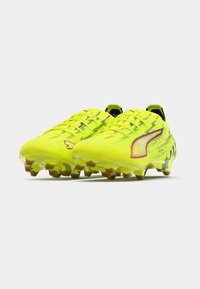 Botas de fútbol de color amarillo brillante con superficie texturizada, detalles en negro y un diseño elegante. Cuenta con cierre de cordones y suela con tacos para tracción.