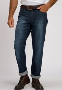 Jeans de denim azul oscuro con corte recto, puños enrollados, cinturón de cuero marrón y botas de cordones marrones, con bolsillos estándar y una textura sutil.