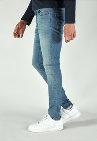 Light blue skinny jeans feature a smooth denim texture, five pockets, and a front button closure, paired with white Nike sneakers.