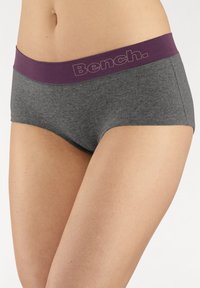 Graue Baumwollslip mit einem breiten lila Bündchen, das das "Bench."-Logo in helllila trägt. Glatte Textur und hipsterartig geschnitten.