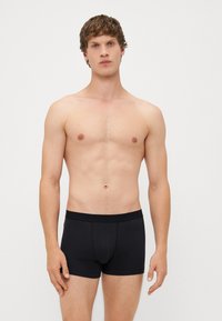 Černé bavlněné boxerky s přiléhavým střihem, hladkým povrchem a měkkým pasem. Model stojí bez trička na neutrálním pozadí.