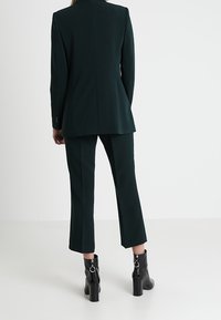 Ciemnozielony garnitur szyty na miarę z dopasowaną marynarką i krotkimi spodniami, w połączeniu z czarnymi botkami za kostkę z zamkiem.