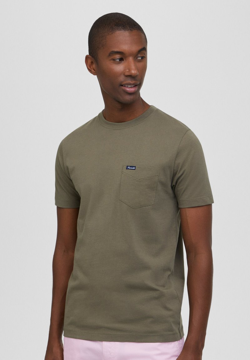 T-shirt in cotone verde oliva con collo rotondo, maniche corte e taschino sul petto. Presenta un piccolo logo blu del marchio sopra la tasca.
