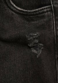 Crne traperice s frayanim otvorom na natkoljenici, vidljivim šavovima i blagim sjajem na tkanini.