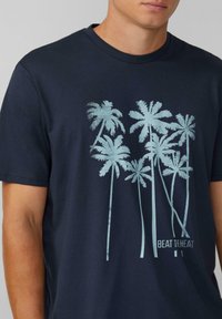 Navyblaue Baumwoll-T-Shirt mit einem hellblauen Palmen-Grafik und dem Text "BEAT THE HEAT" darunter. Kurze Ärmel und runder Ausschnitt.