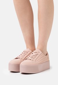 Baskets compensées rose pâle avec une semelle en caoutchouc texturée, une tige synthétique lisse et un design classique à lacets. Finitions discrètes par des surpiqûres.