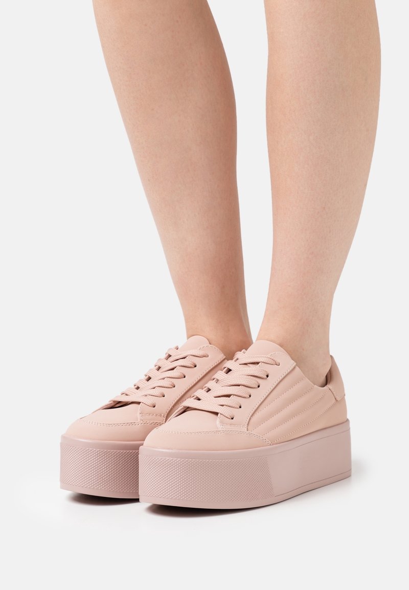 Baskets compensées rose pâle avec une semelle en caoutchouc texturée, une tige synthétique lisse et un design classique à lacets. Finitions discrètes par des surpiqûres.